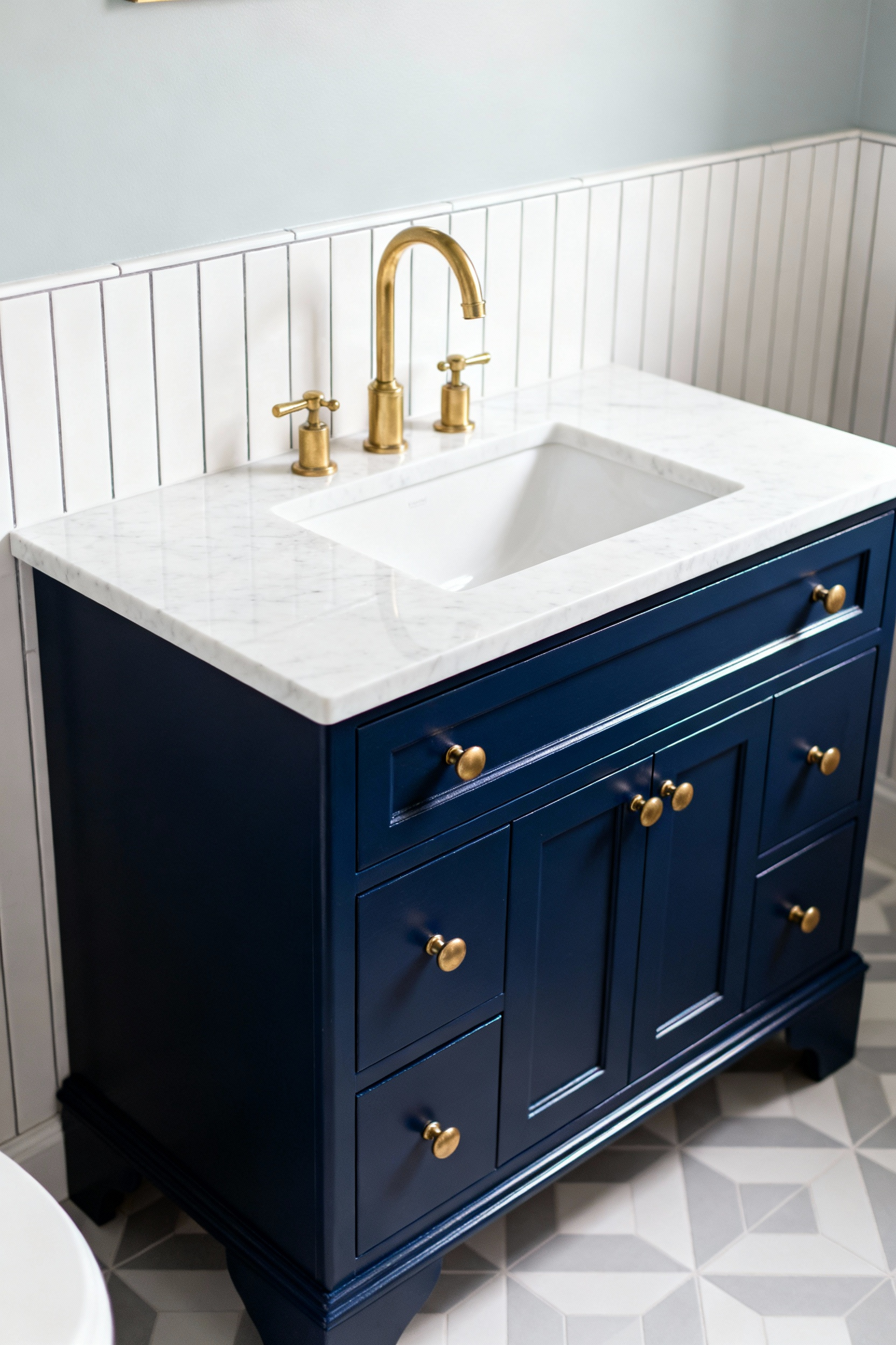 A sustainable bathroom vanity makeover showing a freshly painted navy blue cabinet, contrasted with a white marble countertop and vintage brass pull handles.