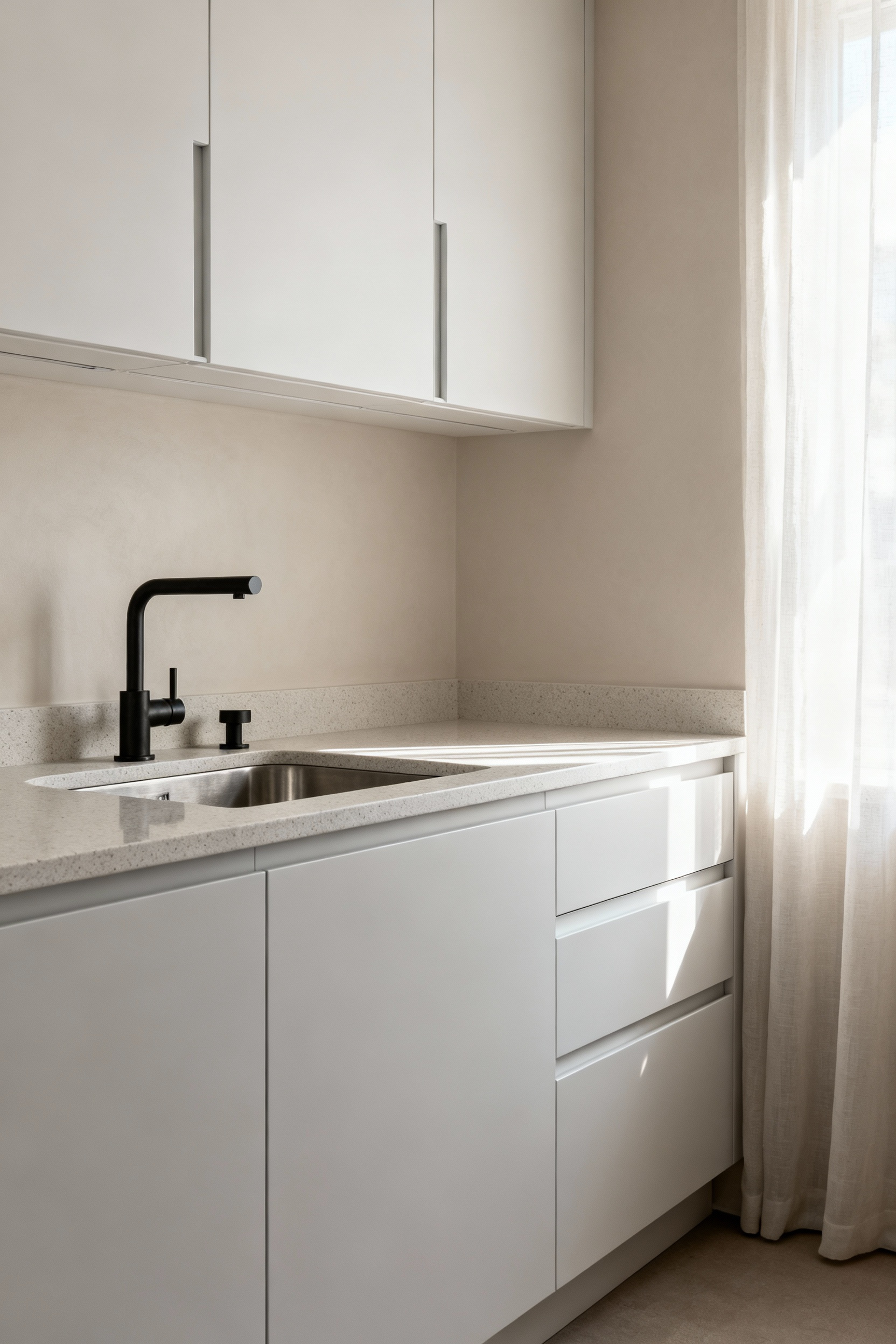 A modern Scandinavian kitchen with matte white cabinets, honed light grey countertops, and brushed metal hardware, showing diffused natural light creating a calm, uncluttered space.