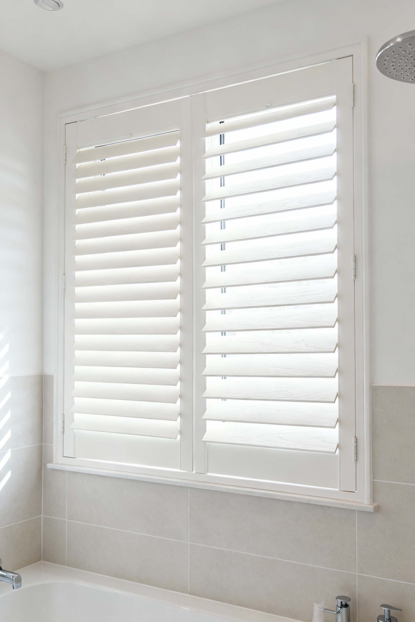 A pristine bathroom window featuring crisp white faux wood blinds, expertly installed, demonstrating superior humidity resilience and a timeless, classic style in a modern bathroom setting.