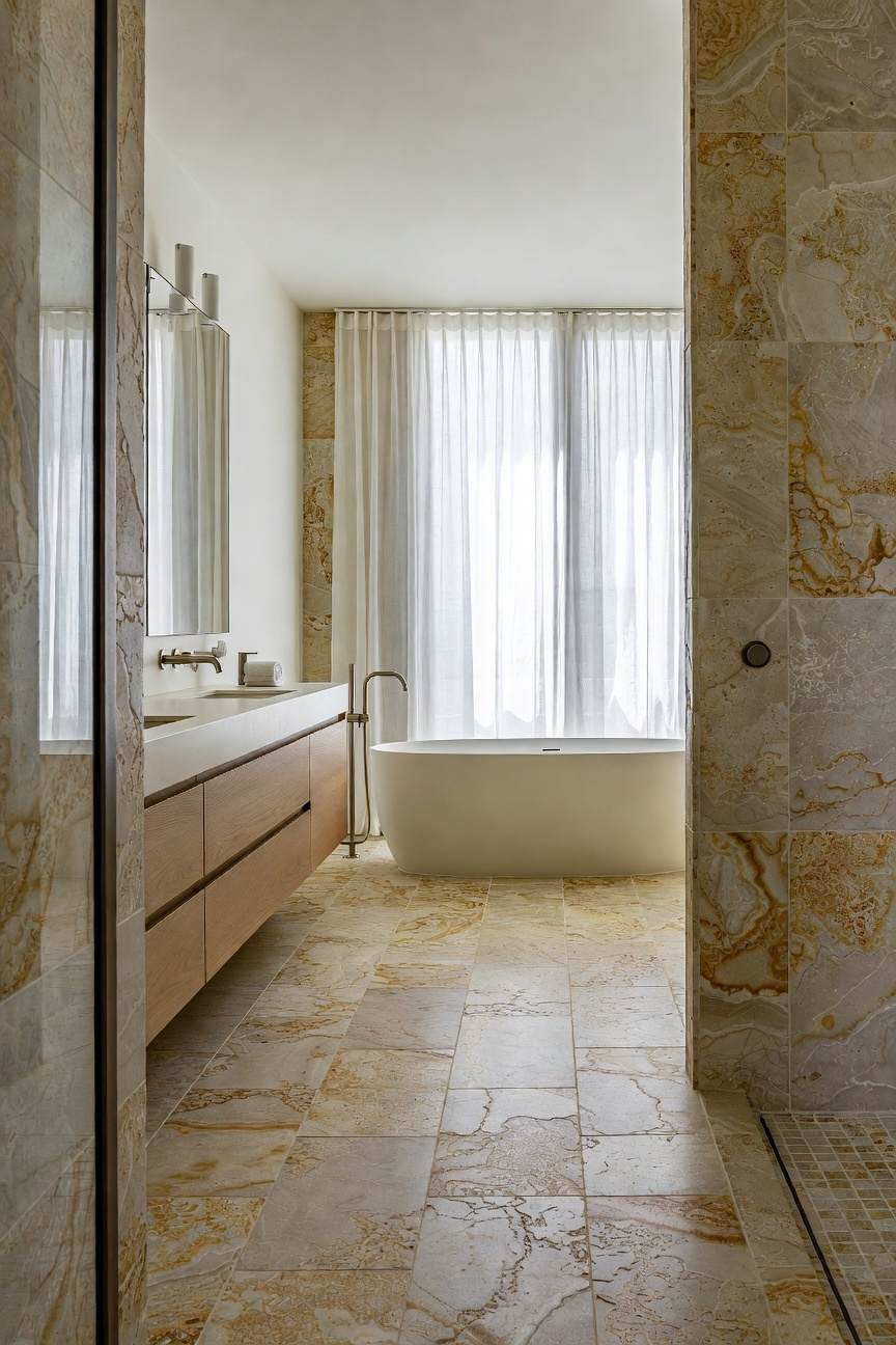 Full interior view of a luxury coastal bathroom showcasing large-format, golden-tan sandstone tiles on the floor and walls, designed to mimic an unbroken shoreline.
