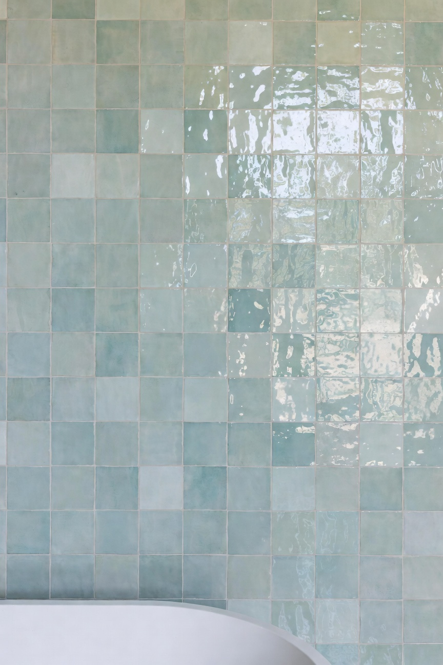 Hand-glazed seafoam green Zellige tiles installed on a coastal bathroom wall reflecting bright natural light and showcasing unique tonal variation and movement.