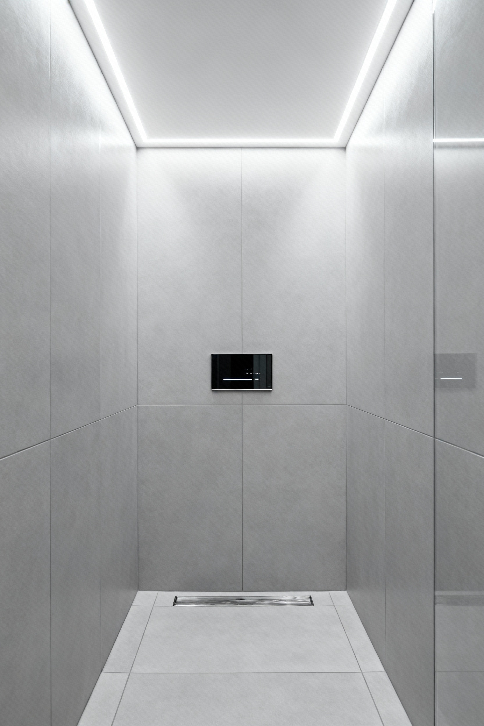 A high-end, minimalist small shower features an ultra-thin digital smart water valve interface mounted flush against large format gray tiles, illustrating how remote mechanical plumbing saves critical wall depth in compact renovations.