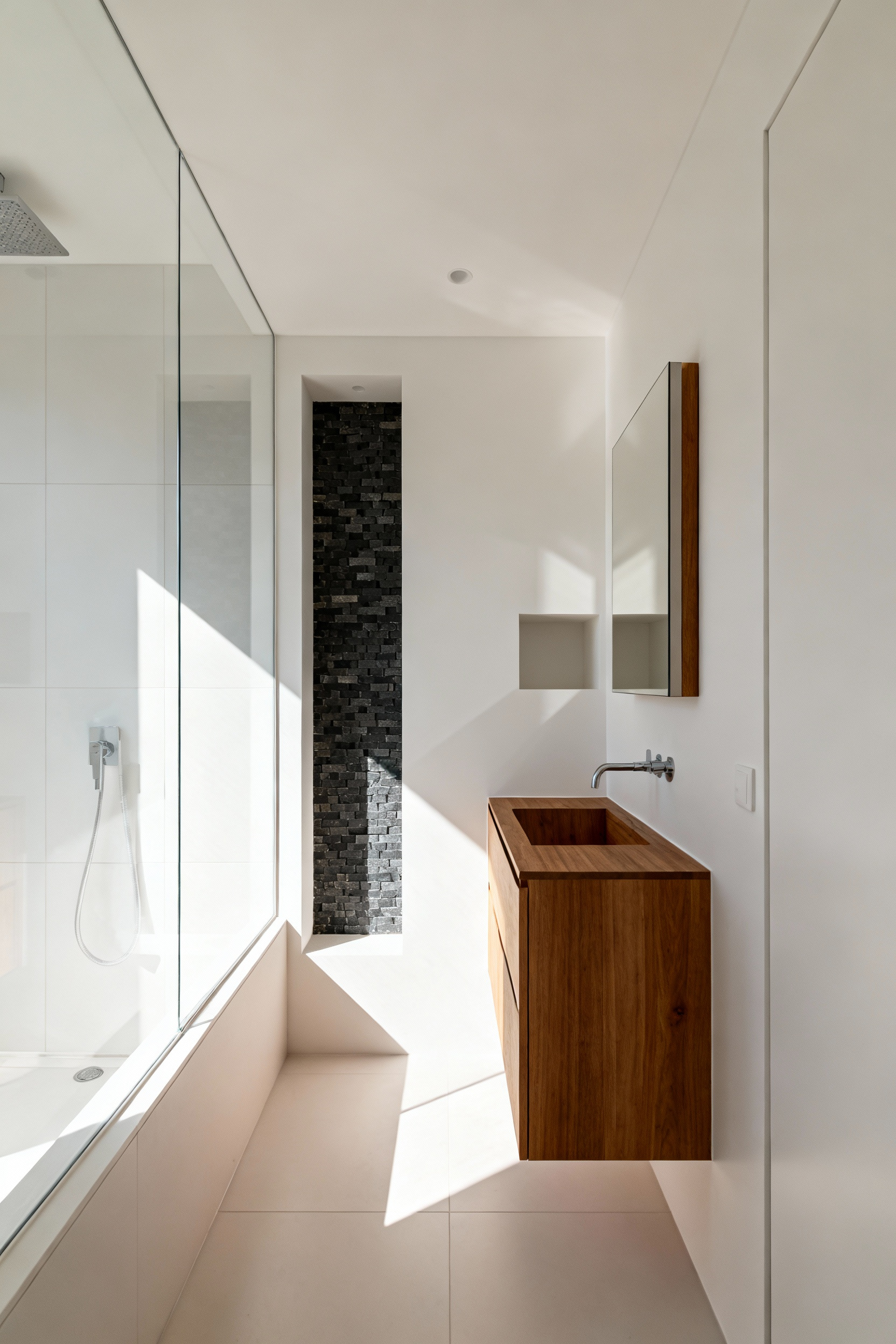 A photograph of a bright, small modern bathroom showing a recessed shower niche and a frameless recessed medicine cabinet, illustrating space maximization by utilizing wall stud cavities.